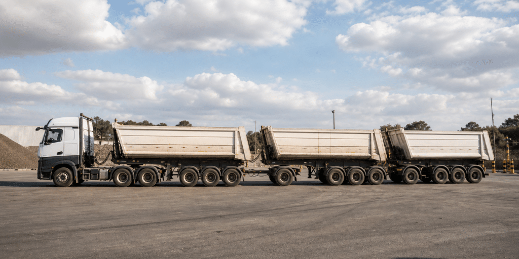 Composição rodoviária longa e articulada em pátio industrial, representando configuração de rodotrem. - diferença entre bitrem e rodotrem.