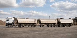 Composição rodoviária longa e articulada em pátio industrial, representando configuração de rodotrem. - diferença entre bitrem e rodotrem.